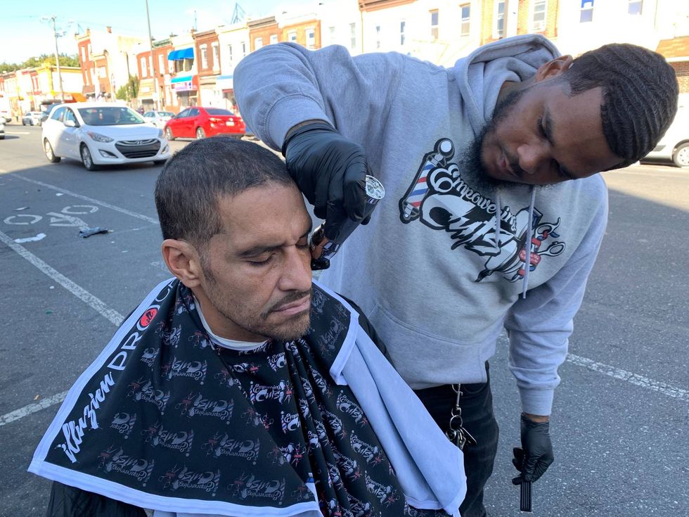 Joshua Santiago gives Angel Ramirez a haircut while other men gather to wait their turn.