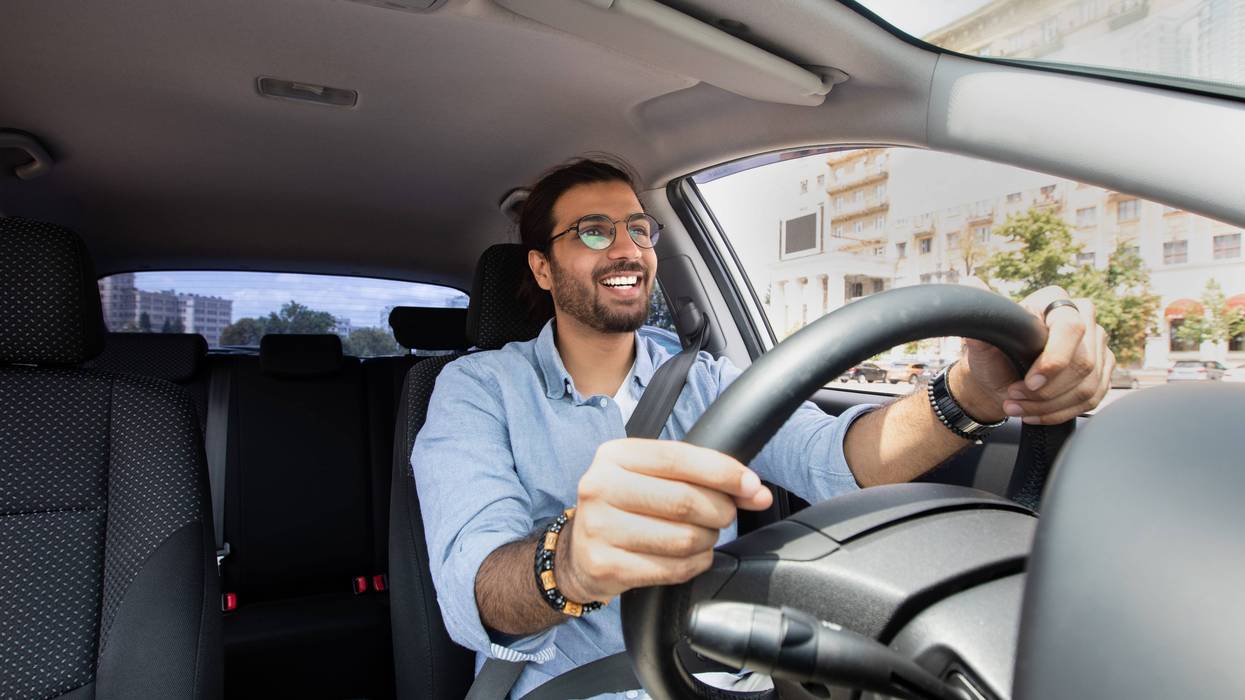 Joyful indian man driving car, shot from dashboard, going on trip during summer vacation, copy space. Happy middle-eastern guy in casual outfit and glasses driving his brand new nice car