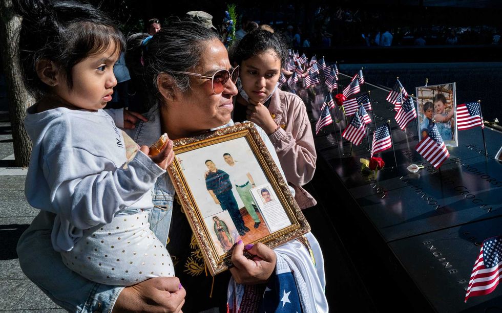 Julia Melendez, holding the photo of her husband Antonio, who died working at Windows on the World restaurant during the attacks of Sept. 11, 2001, holds her granddaughter Scarlet, left, and Darlene, during a ceremony at the 9/11 Memorial and Museum on September 11, 2021 in New York City