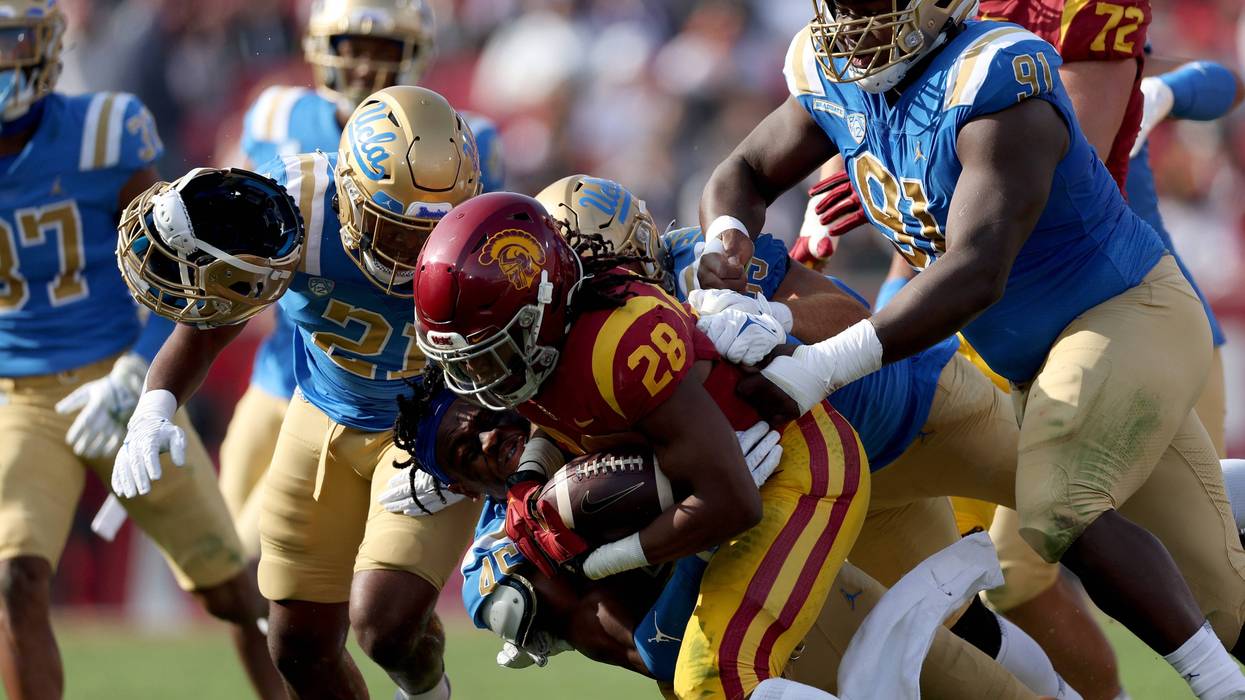 Keaontay Ingram #28 of the USC Trojans rushes as he is tackled by Mitchell Agude #45 of the UCLA Bruins, losing his helmet, during the first quarter at Los Angeles Memorial Coliseum on November 20, 2021 in Los Angeles, California.
