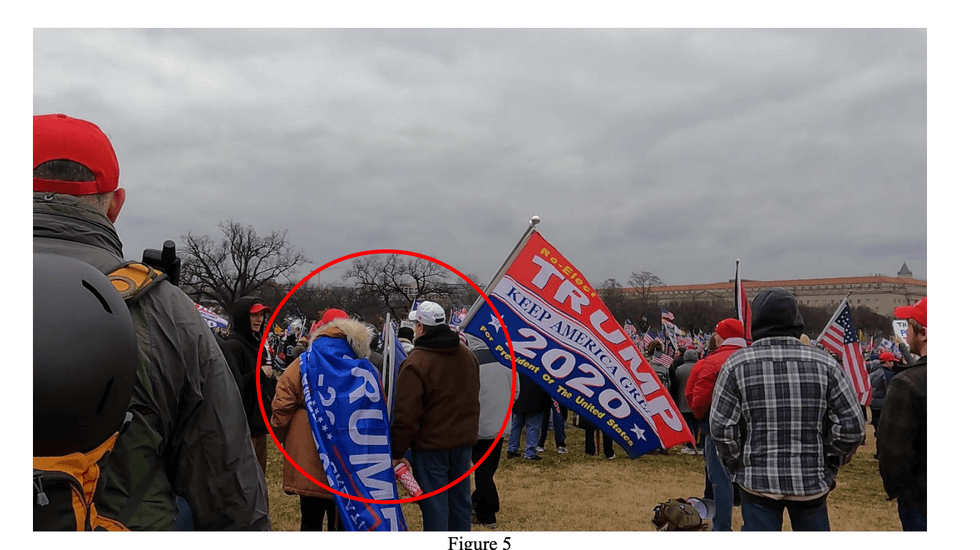 Kevin Moore allegedly wore a white cap, brown hooded jacket, blue jeans, and carried a re-elect Trump flag on Jan 6, 2021.