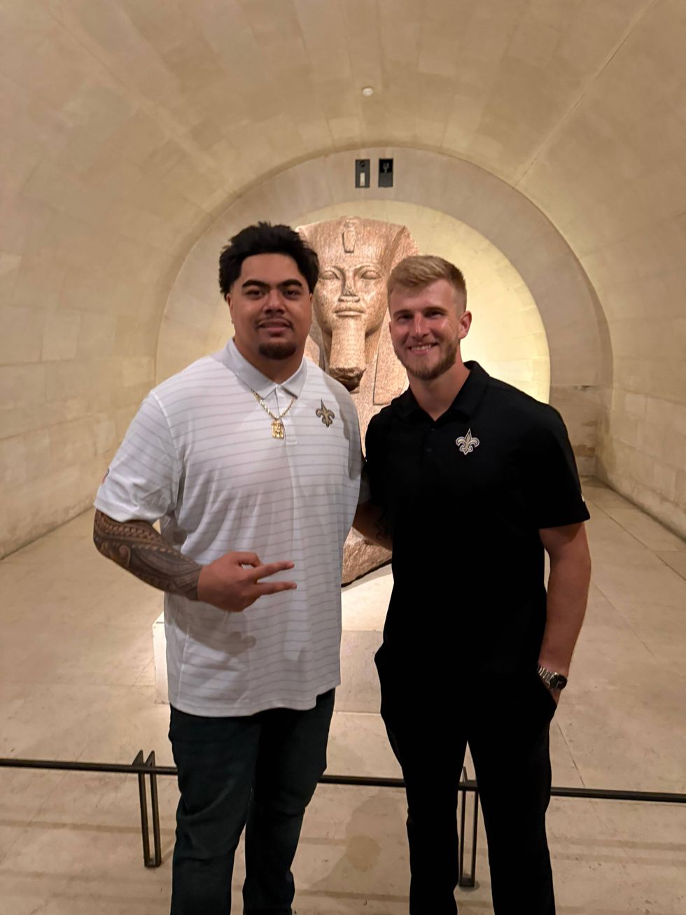 Khalen Saunders & Derek Carr smile in Saints polos in front of an ancient Egyptian pharaoh statue.
