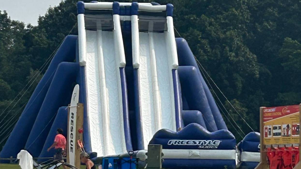 Large blue & white inflatable water slide on a sandy beach with people and life jackets.