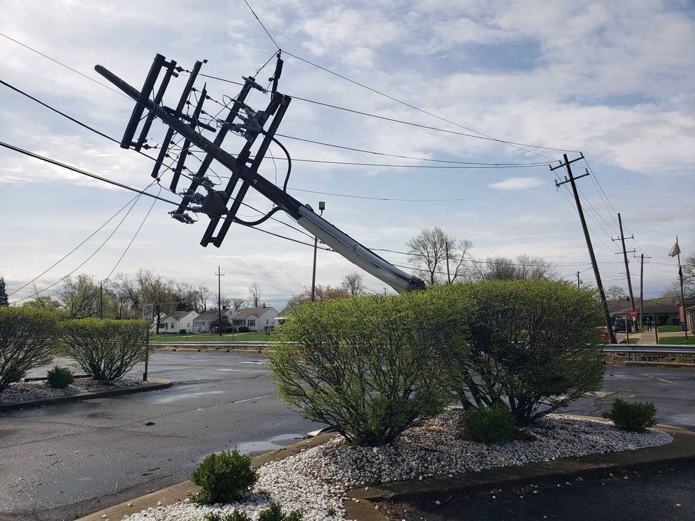 Large utility pole snapped in half, leaning over a parking lot with power lines stretched.