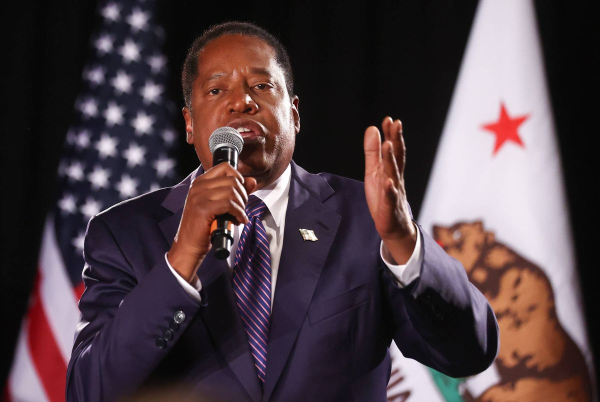 larry elder speaks into microphone before US flag and california flag