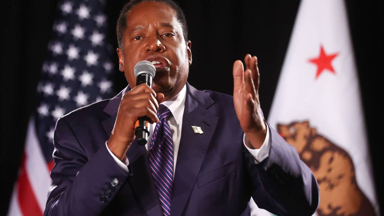 larry elder speaks into microphone before US flag and california flag