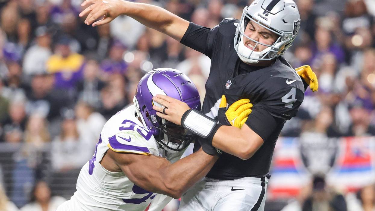 Las Vegas Raiders' QB Aidan O'Connell takes a hit while throwing a pass against the Minnesota Vikings.