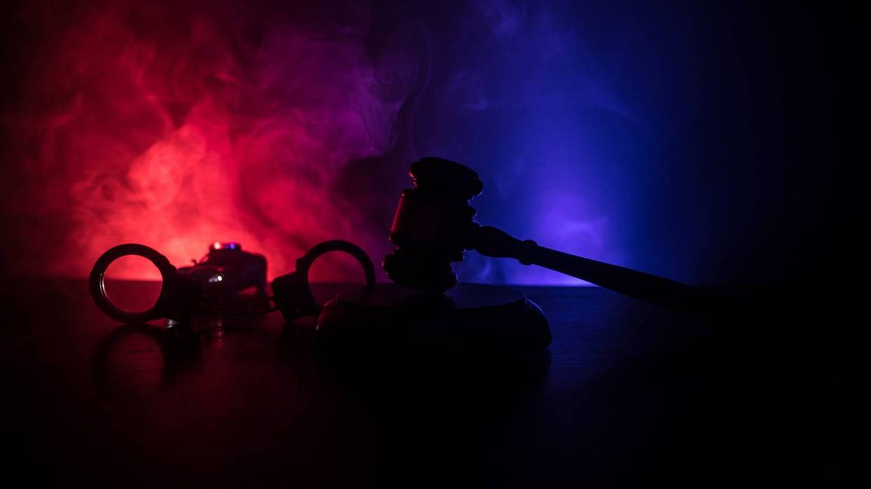 Law theme, mallet of the judge on wooden desk with Lady Justice Statue. Silhouette of handcuffs with police car on backside. Law gavel on dark foggy background with light.
