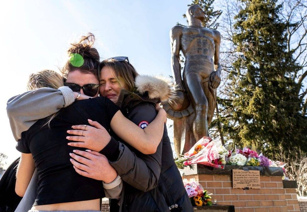 (Left to right) Michigan State University junior Tori VanSlambrouck of Kalamazoo is hugged by senior Alix Matzke of Cadillac and junior Emily Finkbeiner of Saline after they left flowers at the base of the Sparty statue following an active shooting incident on the Michigan State University campus in East Lansing on Tuesday, February 14, 2023, that left three people dead and multiple injured.