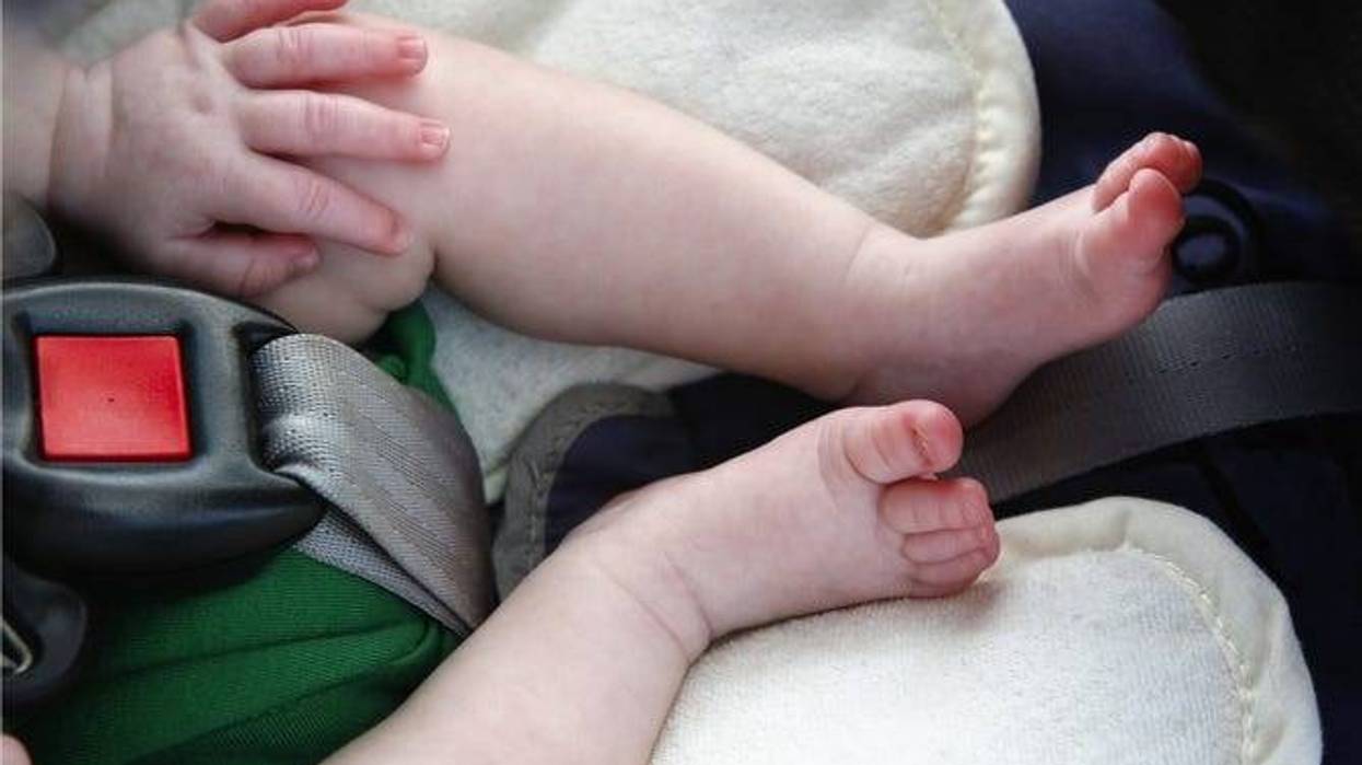 Legs and hand of little child in car seat.
