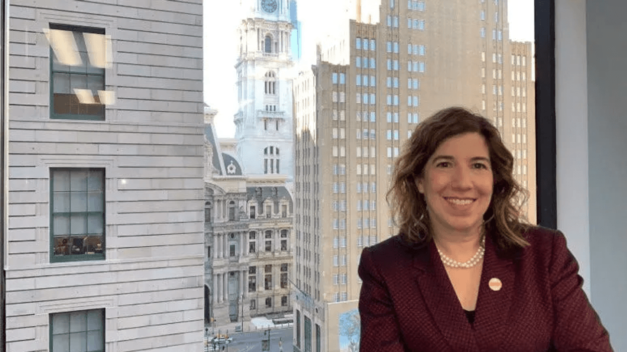 Leslie Richards poses in front of a window with Philadelphia City Hall in the background.
