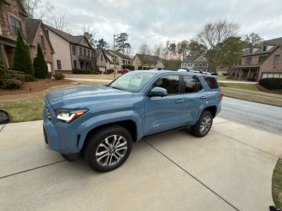 Light blue Toyota 4Runner SUV with roof racks parked on a suburban driveway in front of houses.