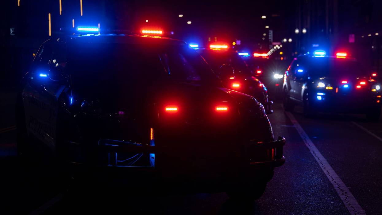 Line of police cars with flashing red and blue emergency lights in the dark.