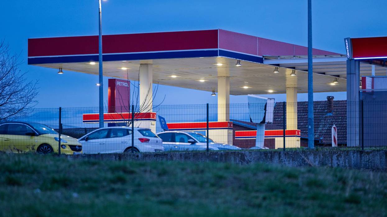 Lit gas station with red and blue canopy at dusk, cars visible.