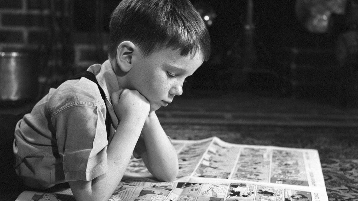 Little boy reading his paper's comic section.