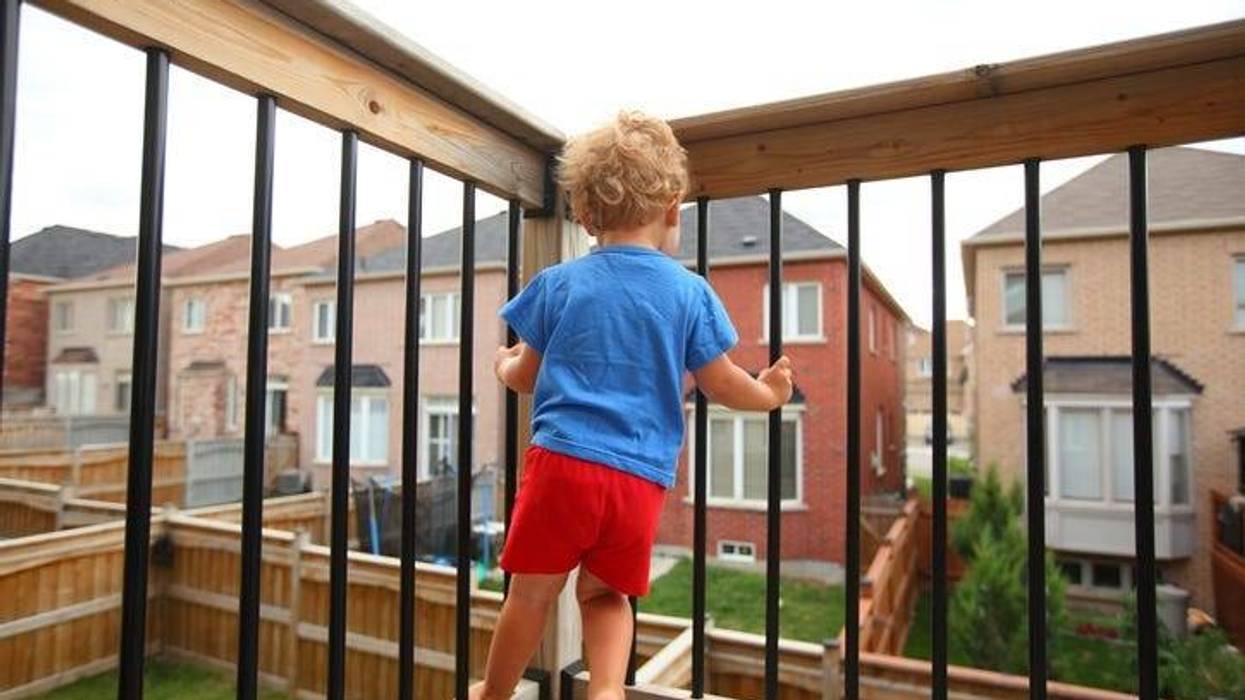 Little boy standing on the balcony (patio) above the ground and trying to climb on balcony railing. House living and child-proofing