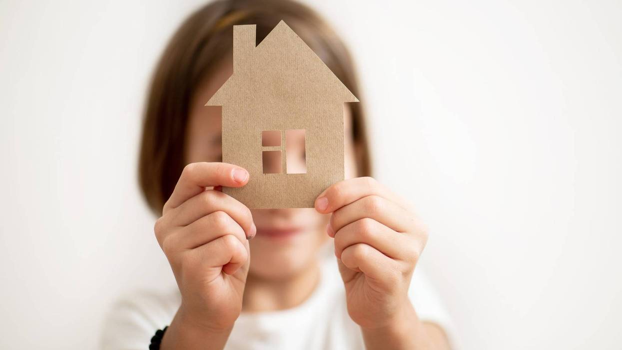 Little girl holding paper house in front of her face.