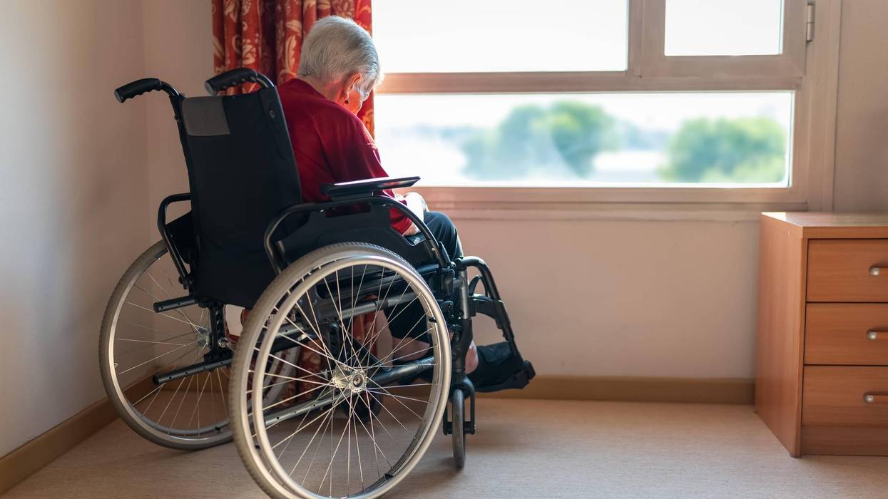 Lonely older woman sitting in a wheelchair in front of a window