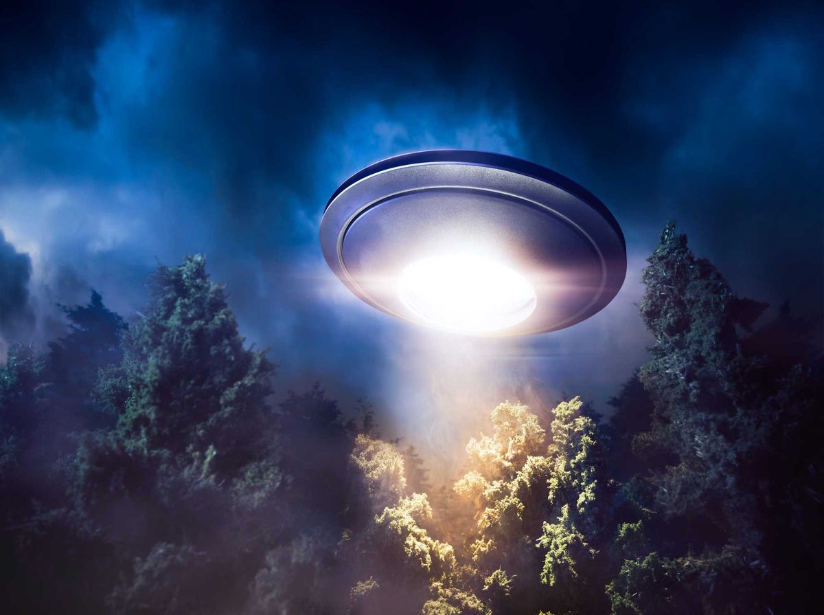 low key image of UFO hovering over a forest at night