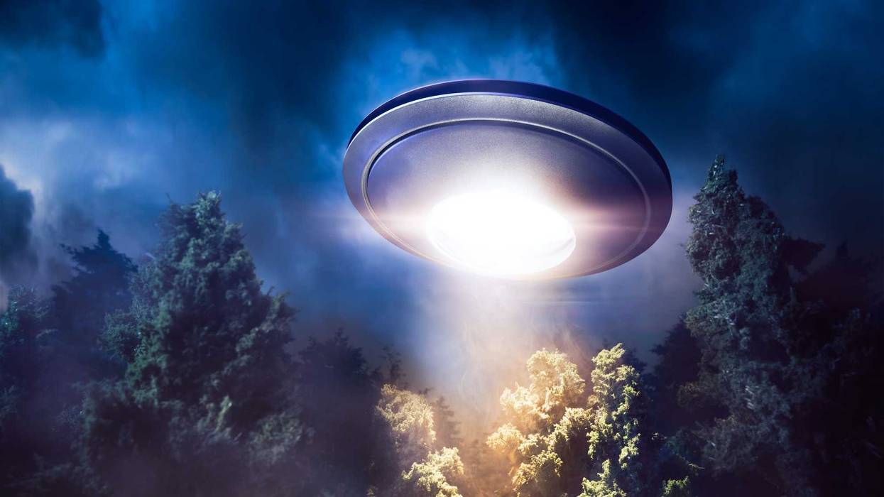 low key image of UFO hovering over a forest at night
