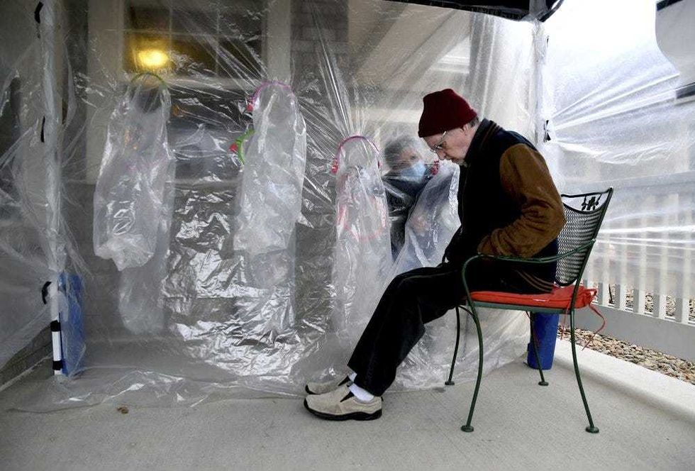 Lynda Hartman, 75, background, visits her 77-year-old husband, Len Hartman, in a "hug tent" set up outside the Juniper Village assisted living center in Louisville, Colo., Wednesday, Feb. 3, 2021. The tent includes a construction-grade plastic barrier with built-in plastic sleeves to prevent the spread of the coronavirus. Len Hartman suffers from dementia and has been living at the center for about a year. The couple had not had any physical contact for at least eight months.