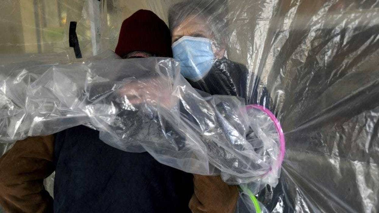 Lynda Hartman, 75, embraces her 77-year-old husband, Len Hartman, who suffers from dementia in a "hug tent" set up outside the Juniper Village assisted living center in Louisville, Colo., Wednesday, Feb. 3, 2021. The tent includes a construction-grade plastic barrier with built-in plastic sleeves to prevent the spread of the coronavirus. He has been living at the center for about a year, and the couple had not had any physical contact for at least eight months.