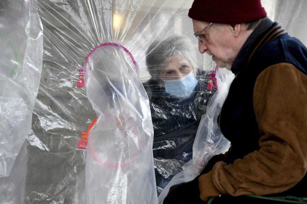 Lynda Hartman, 75, visits her 77-year-old husband, Len Hartman, in a "hug tent" set up outside the Juniper Village assisted living center in Louisville, Colo., on Wednesday, Feb. 3, 2021. The tent includes a construction-grade plastic barrier with built-in plastic sleeves to prevent the spread of the coronavirus. Len Hartman suffers from dementia and has been living at the center for about a year. The couple had not had any physical contact for at least eight months. (AP Photo/Thomas Peipert)