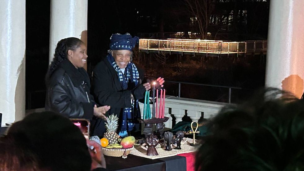 Maisha Sullivan-Ongoza and Milele Sullivan of the Kwanzaa Cooperative light the first candle on the kinara, representing unity.