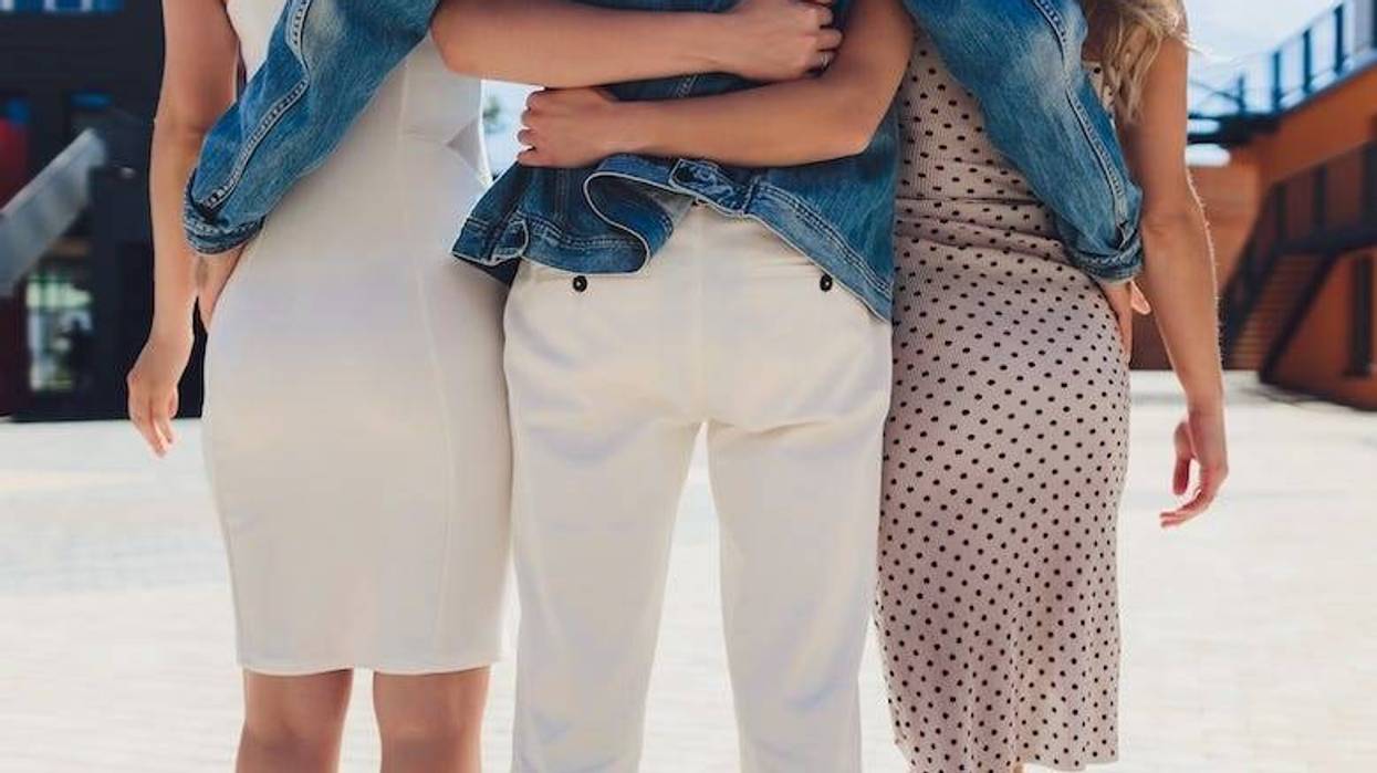Male and two females walking down the street with arms around each other’s backs
