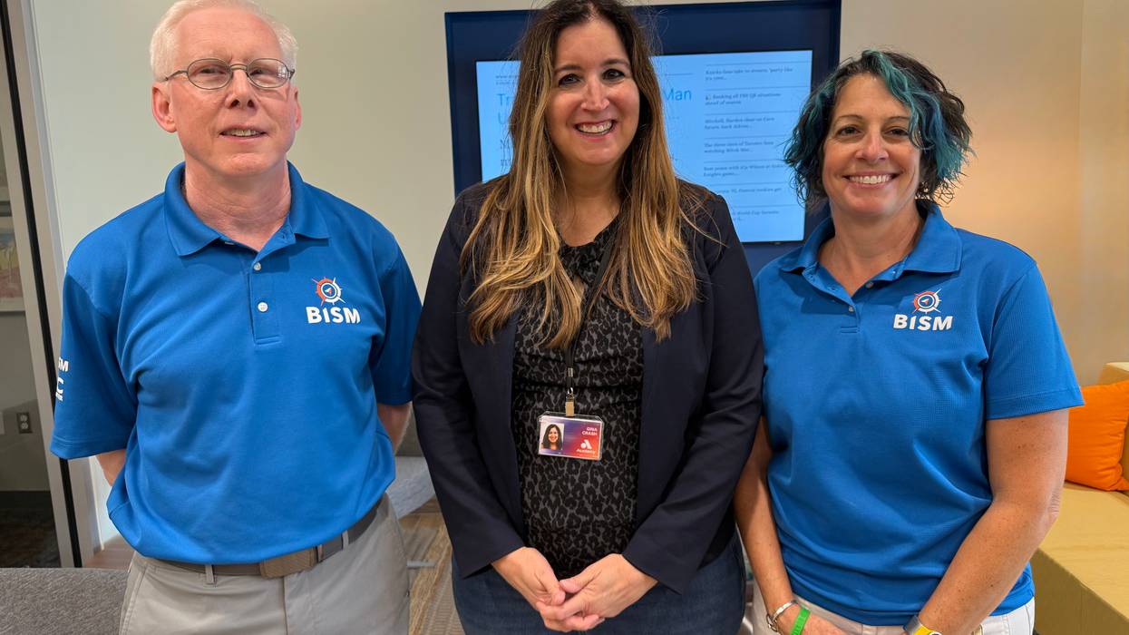 Man and two women, two in blue BISM shirts, smiling for a group photo in an office.