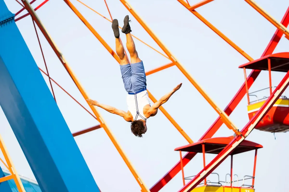 Man diving headfirst, arms spread, against a red and orange Ferris wheel.