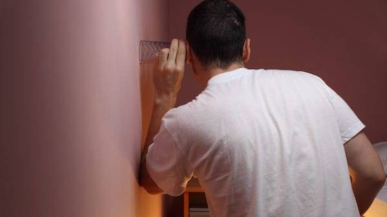 Man eavesdropping through a bedroom wall using a glass
