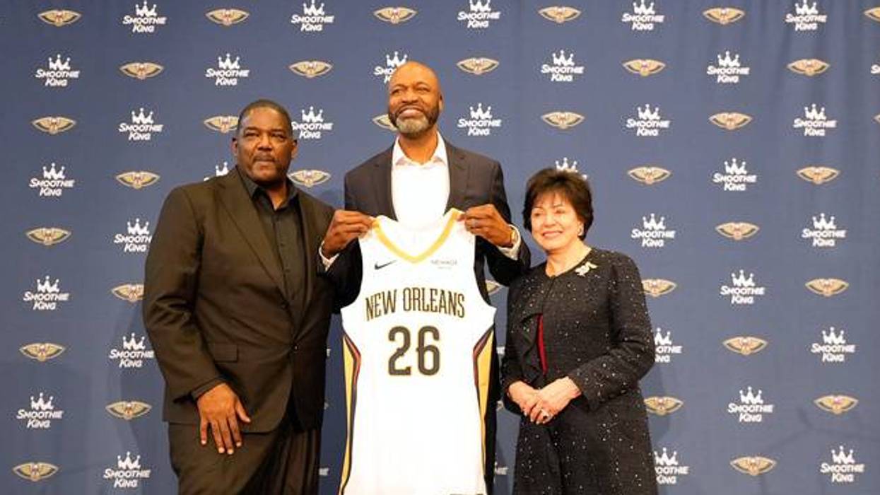 Man holds up New Orleans Pelicans jersey #26, flanked by a man and a woman at team event.