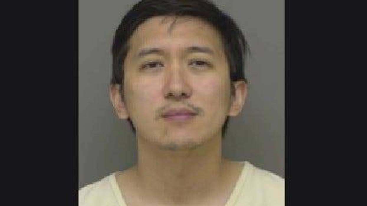 Man in 20s wearing white v-neck with black short hair and small amount of facial hair