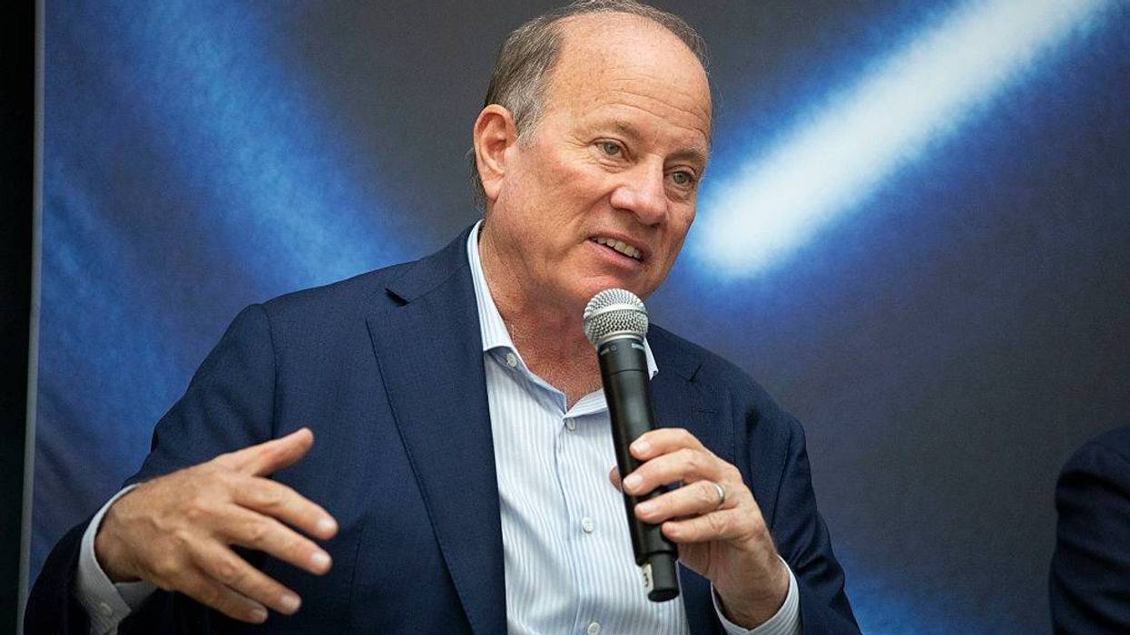 Man in dark suit holds microphone and gestures while speaking.