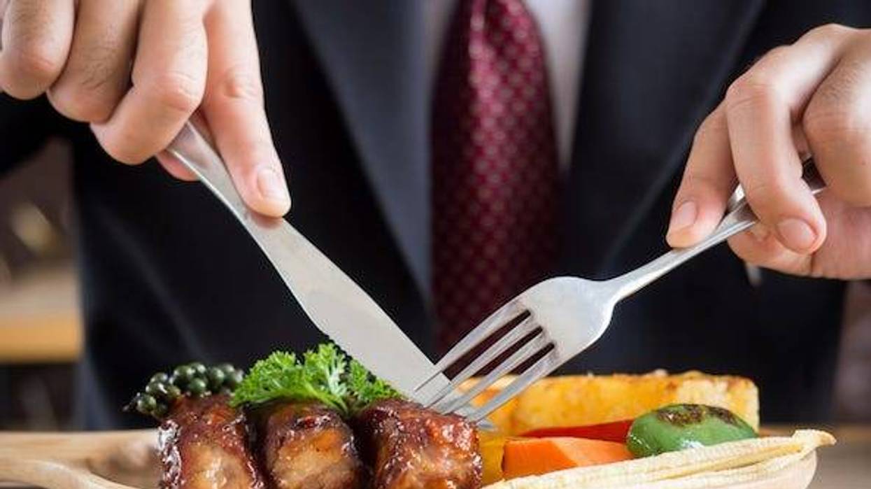Man in suit and tie cutting steak