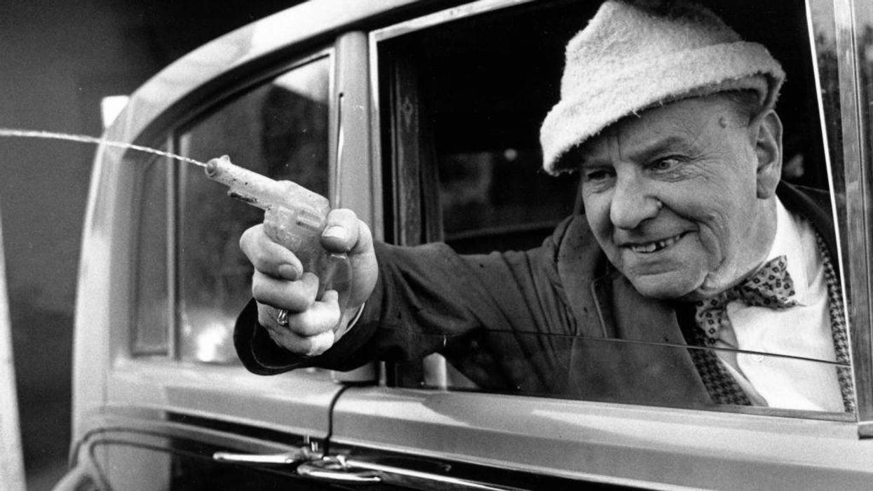 man pointing water gun out of car window