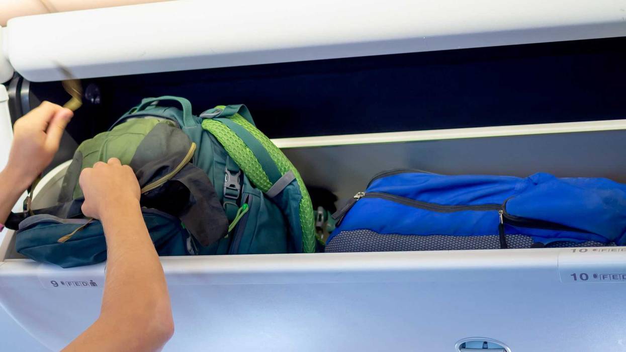 Man putting luggage in overhead airplane compartment stock photo.