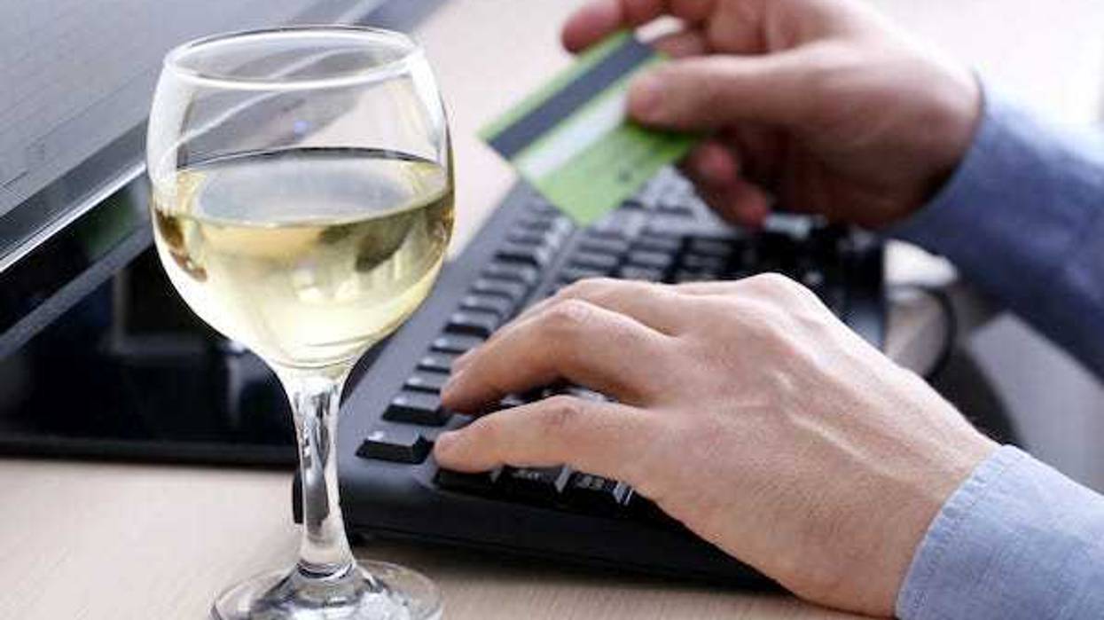 Man typing on a keyboard holding a credit card next to a glass of white wine