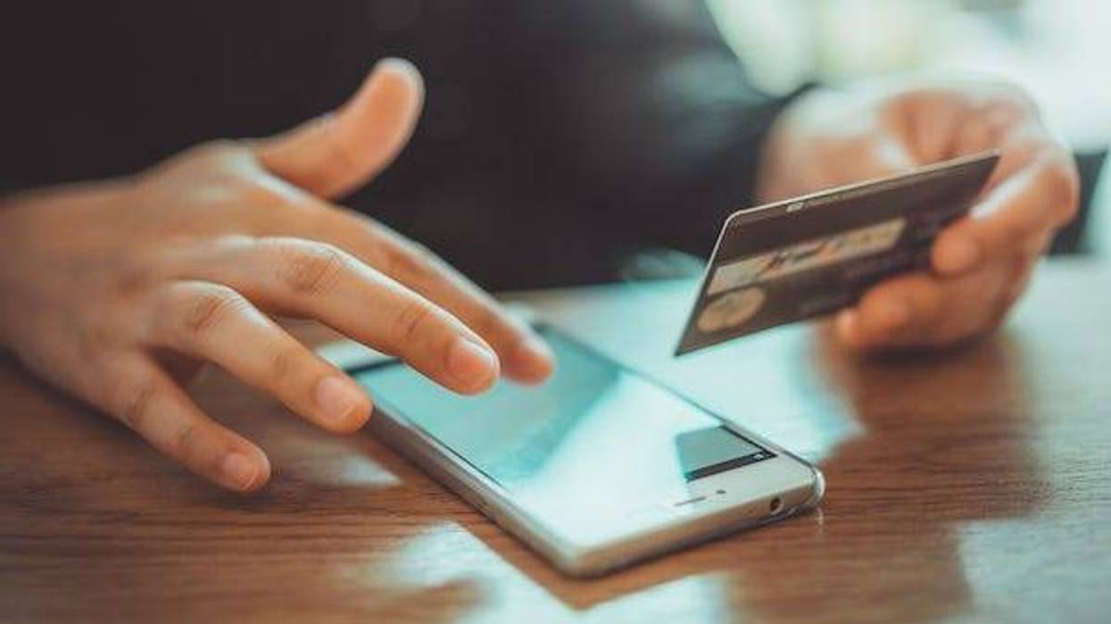 Man typing on his phone while holding his credit card