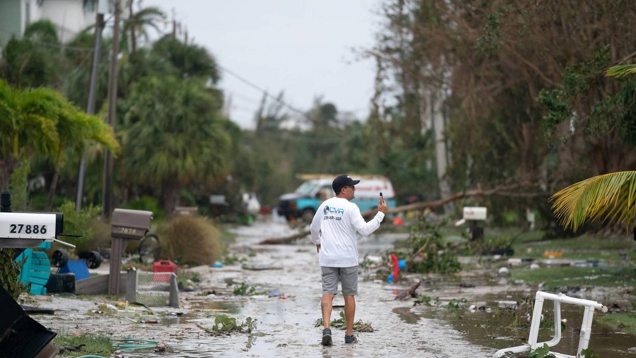 man walks through flooded road full of water and debris surrounded by palm trees