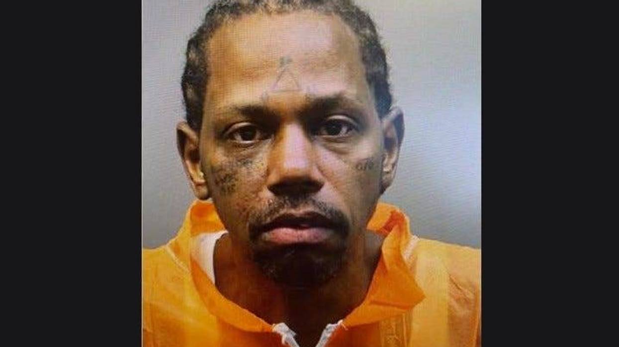 man wearing orange zip up with cornrows and face tattoos in mug shot