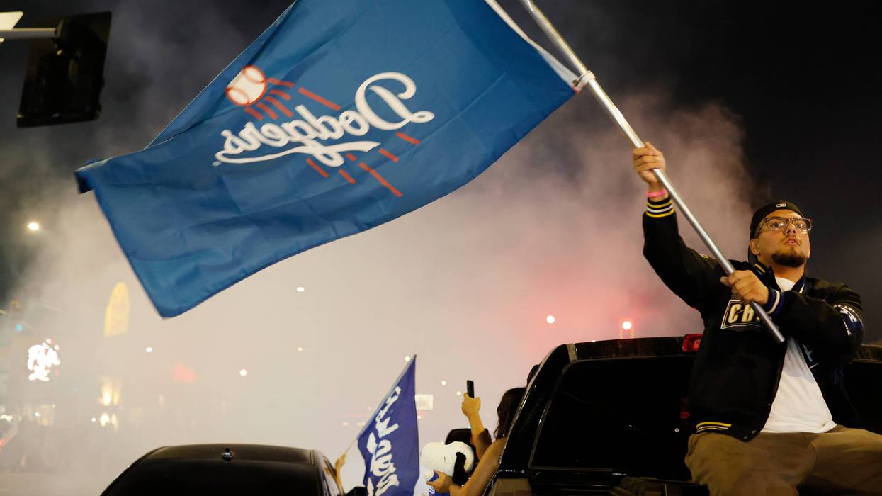man with dodger flag sitting on back of a car