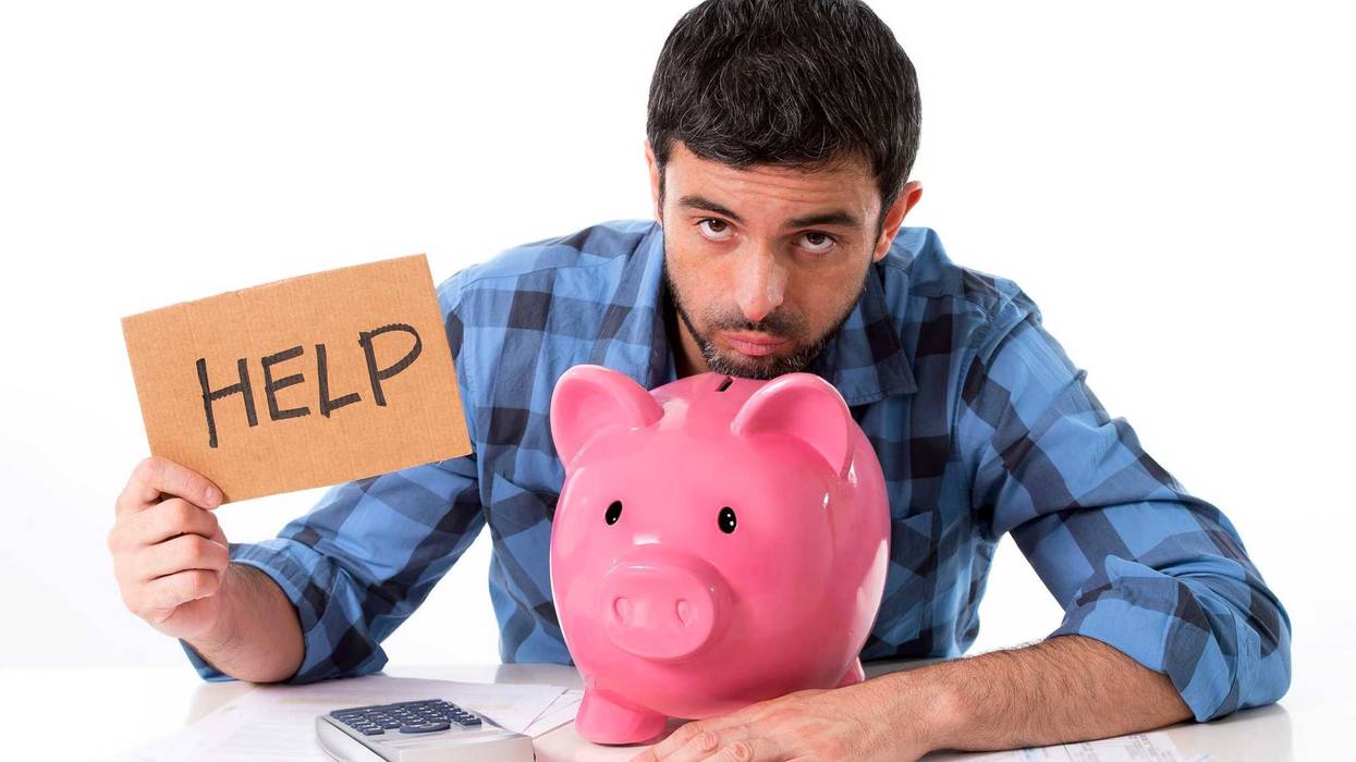 Man with his head resting on a large pink piggy bank holding a sign that reads "help."