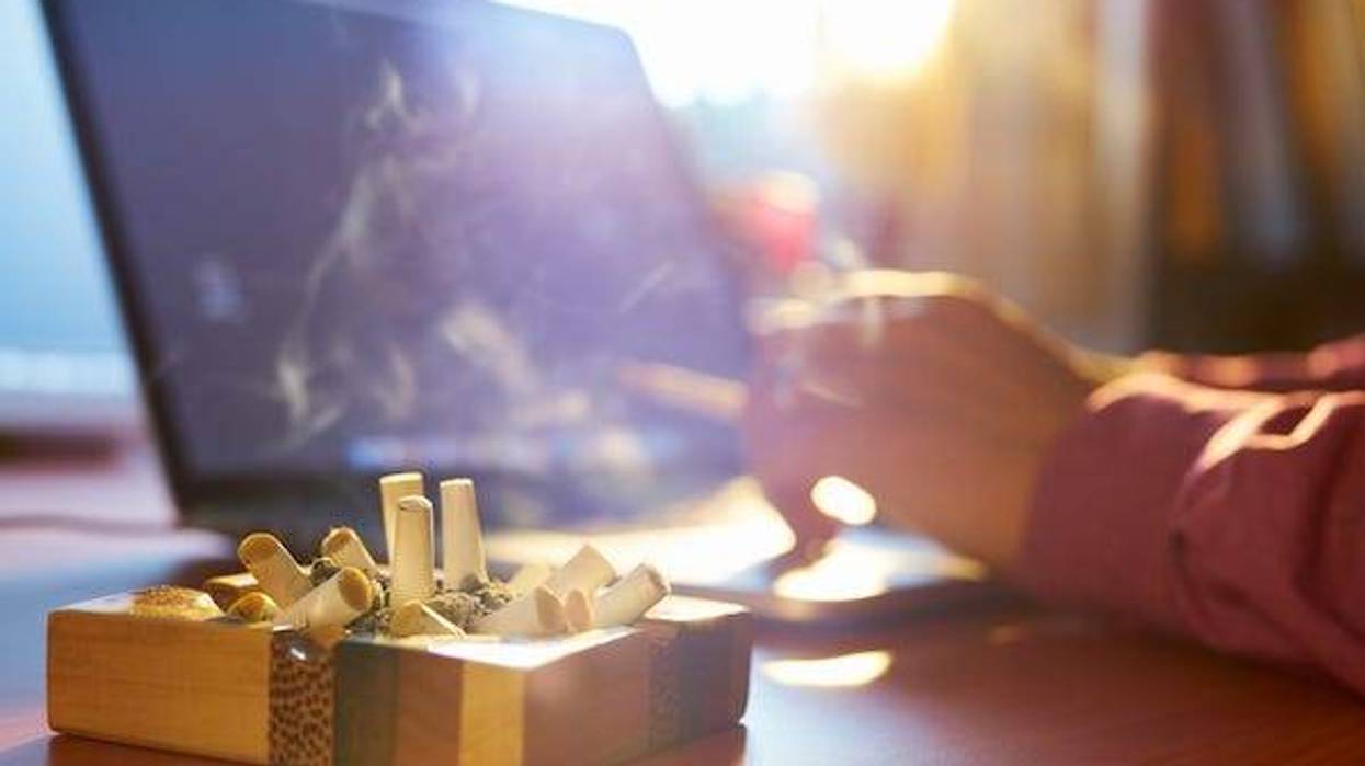 Man working on laptop next to ashtray full of cigarettes