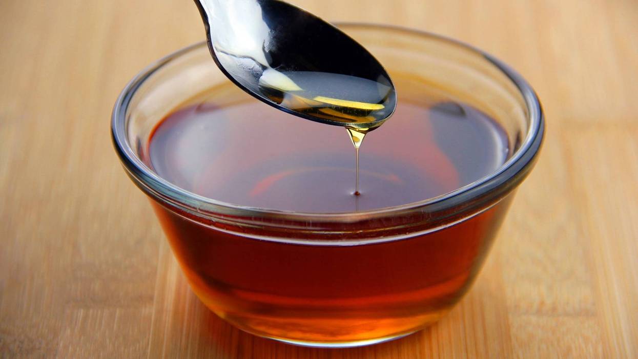 Maple syrup dripping off of a spoon into a glass bowl set on bamboo wooden surface