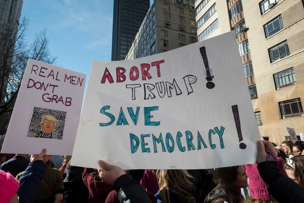 Marchers hold signs that say, "Abort Trump Save Democracy" and "Real Men Dont Grab" walking during the second annual Women
