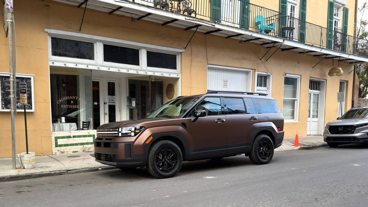 Matte brown SUV parked on a city street in front of a yellow building with a bakery.