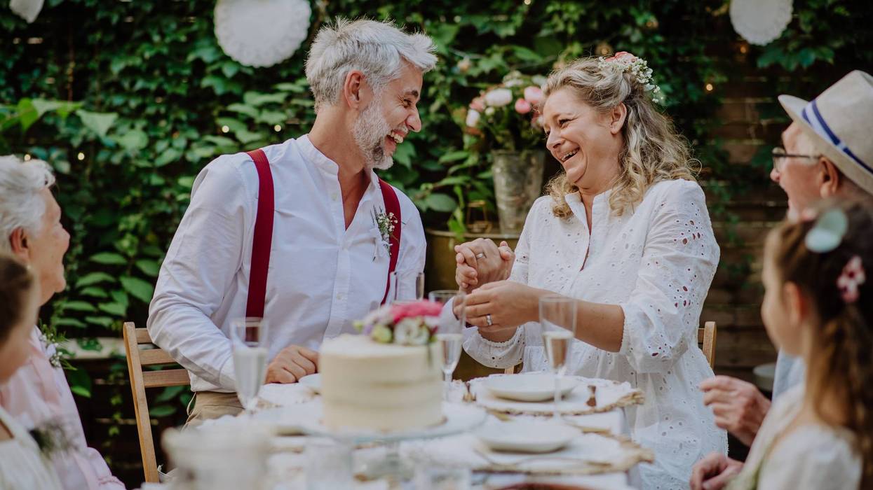 Mature bride and groom with guests at wedding reception outside in the backyard.