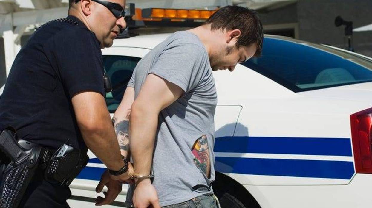 Mature police officer arresting drug dealer with car in the background